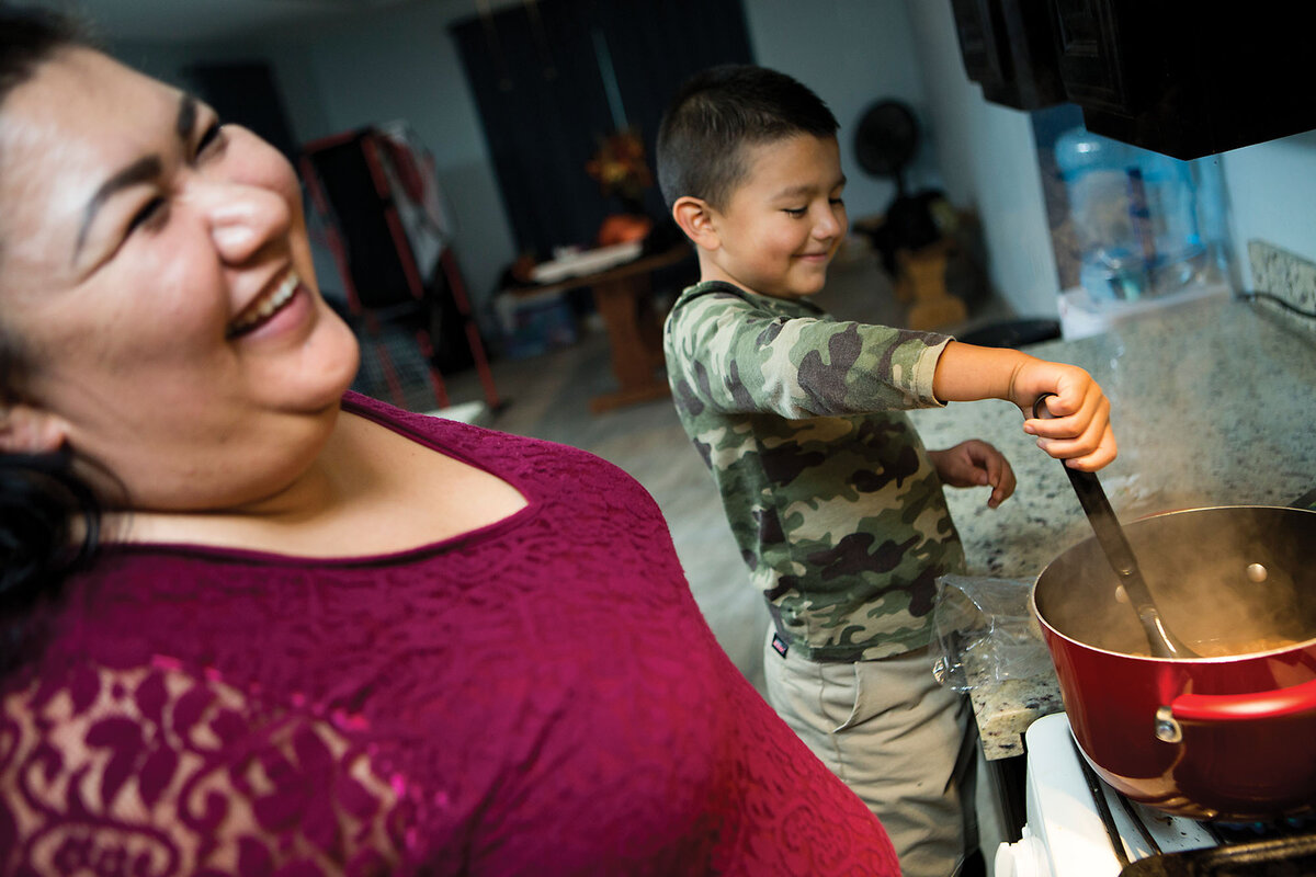 Michelle Salazar smiles as she stands with her son, Mario, in the kitchen while he stirs a pot for their dinner in Donna, Texas, in 2018.