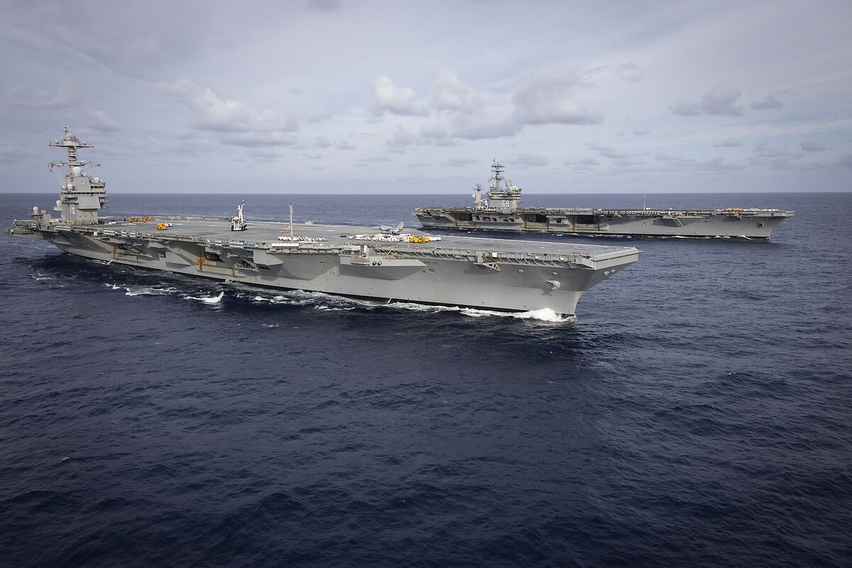 Two aircraft carriers plow through dark ocean water.