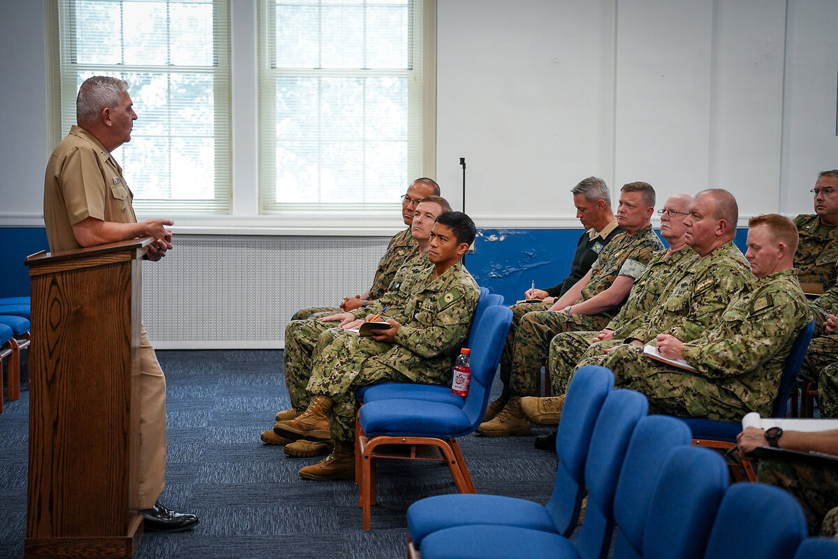 Navy chaplains sit while listening to Rear Adm. Gregory Todd, standing at a podium.
