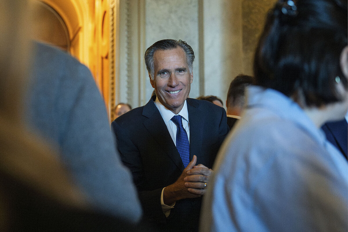 Mitt Romney smiles, standing near news reporters.