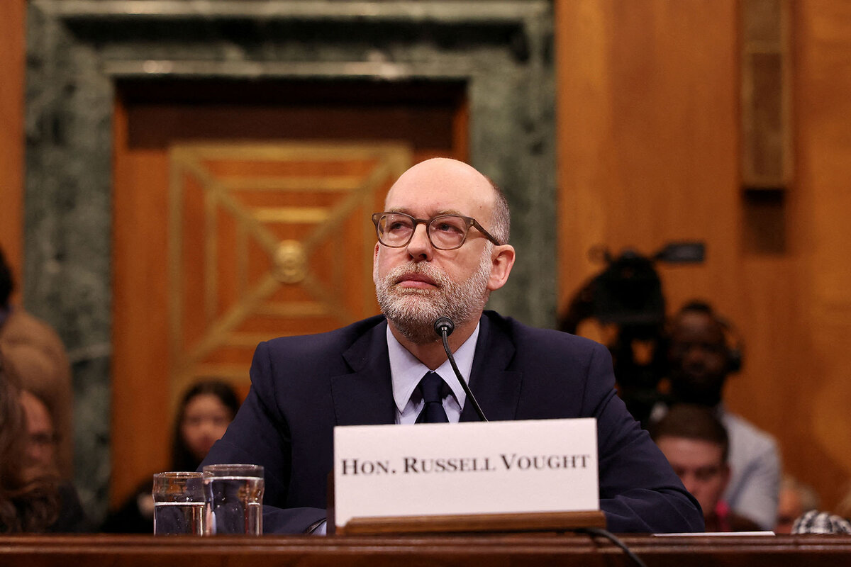 Russell Vought listens while seated during his Senate confirmation hearing.