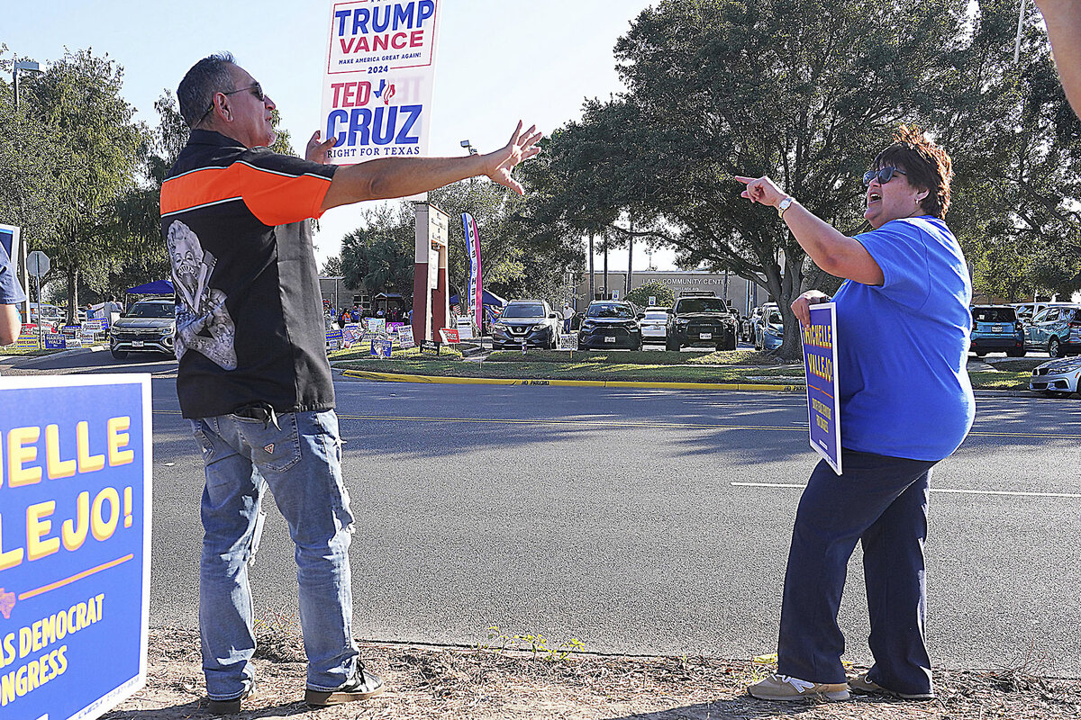 A man stands by the road holding a Trump Vance sign while arguing with a woman wearing a blue shirt who supported Kamala Harris.