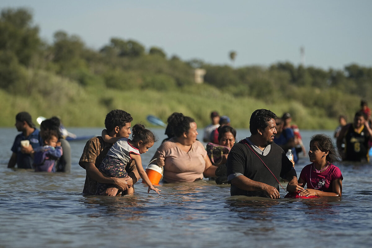 Migrants move around concertina wire along the banks of the Rio Grande after crossing from Mexico into the U.S.