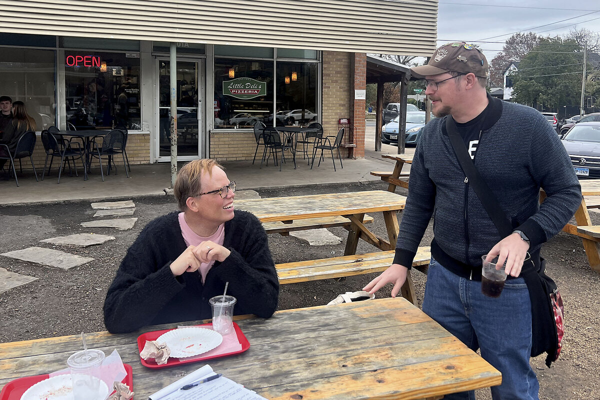 Jeff Hiller sits at a picnic table outside Little Deli & Pizzeria in Austin, Texas. He chats with fellow Texan Jacob Scott, who is standing.