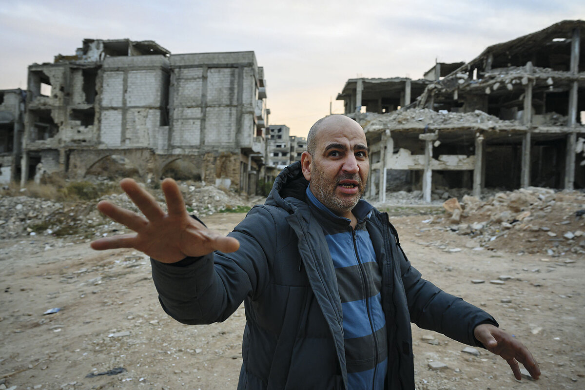 A former rebel fighter motions to the camera destroyed buildings in Homs, Syria.