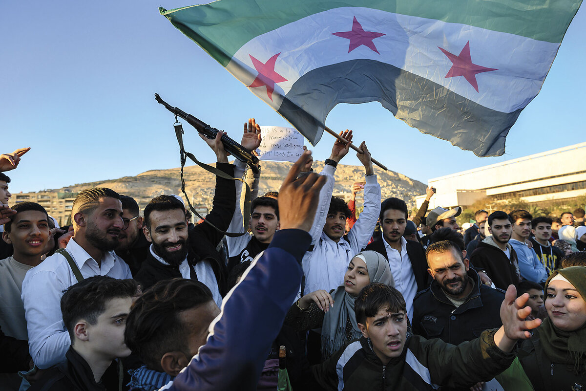 A crowd of young Syrians celebrate smile and celebrate in Damascus. One waves a Syrian flag, another a gun.