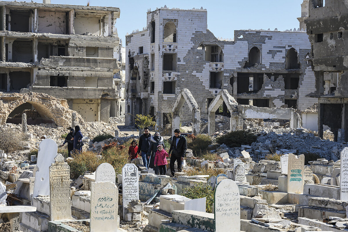 A Syrian family walks through rubble and headstones in a Damascus cemetery.