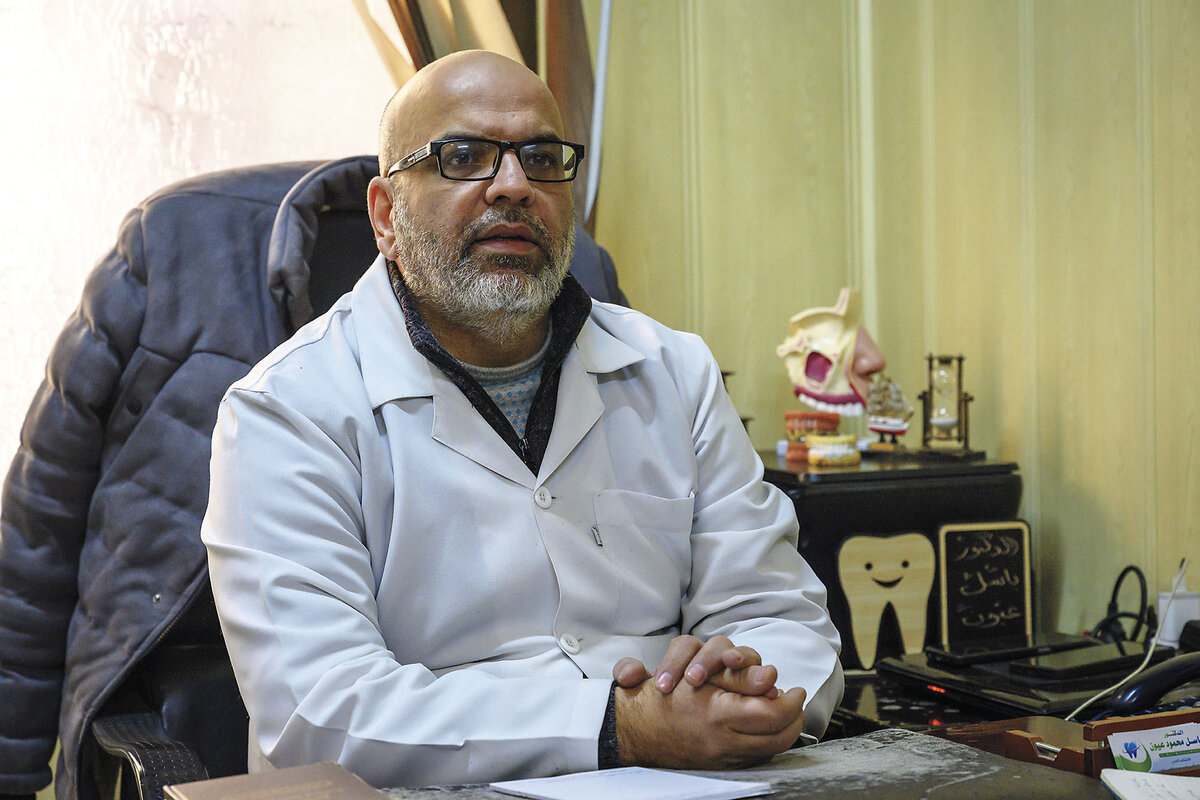 A Syrian dentist sits at a desk with dental paraphernalia in Damascus.