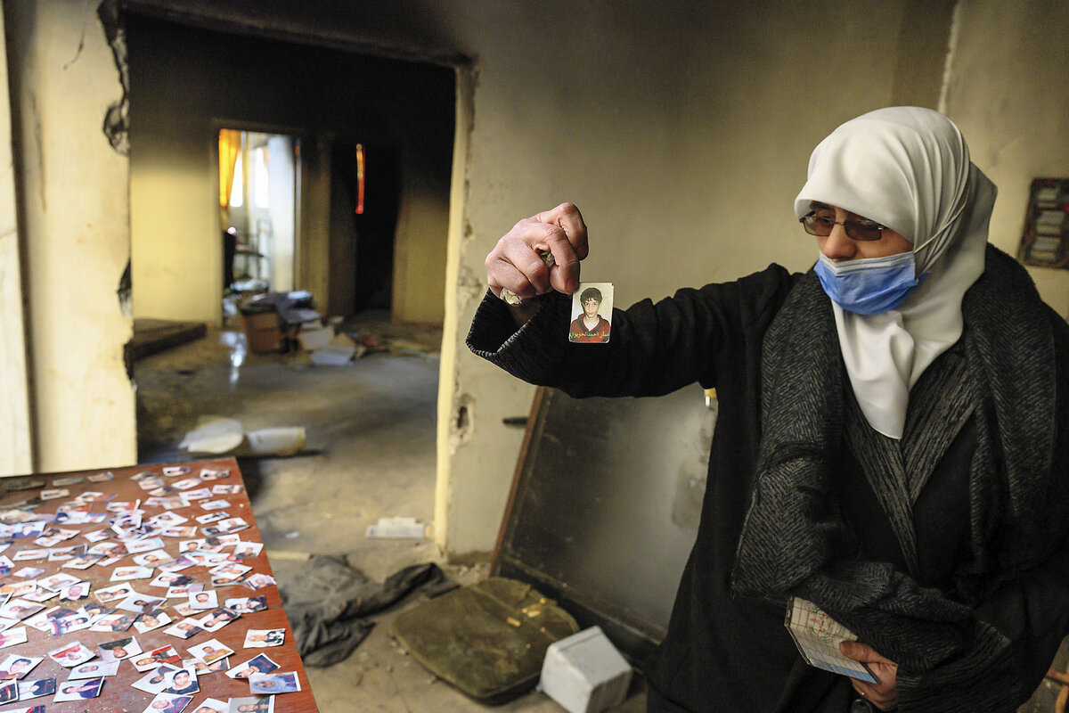 A Syrian woman examines a passport photo in front of a counter splayed with similar photos at Syria’s Palestine Branch prison.