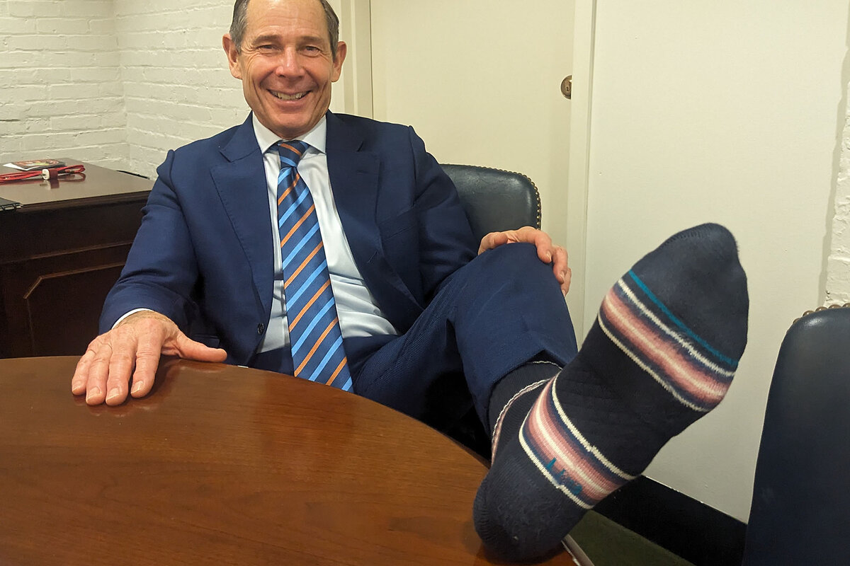 John Curtis, in a suit and tie, extends his foot to show one of his colorful socks.
