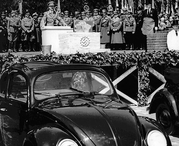 Adolf Hitler stands behind a podium and an early Volkswagen in Wolfsburg, Germany, in 1938.