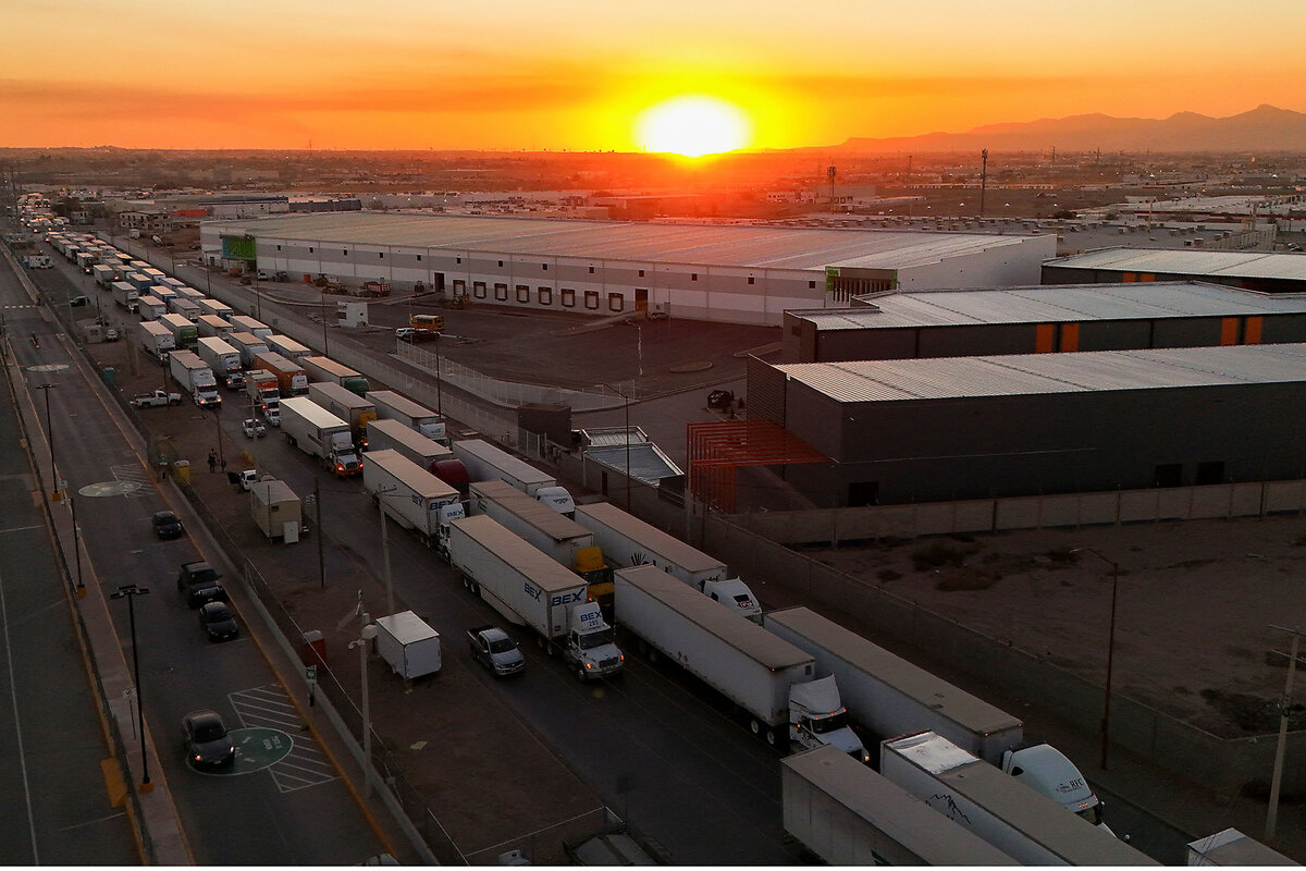 With a setting sun and orange sky in the background, dozens of freight trucks wait in a line.