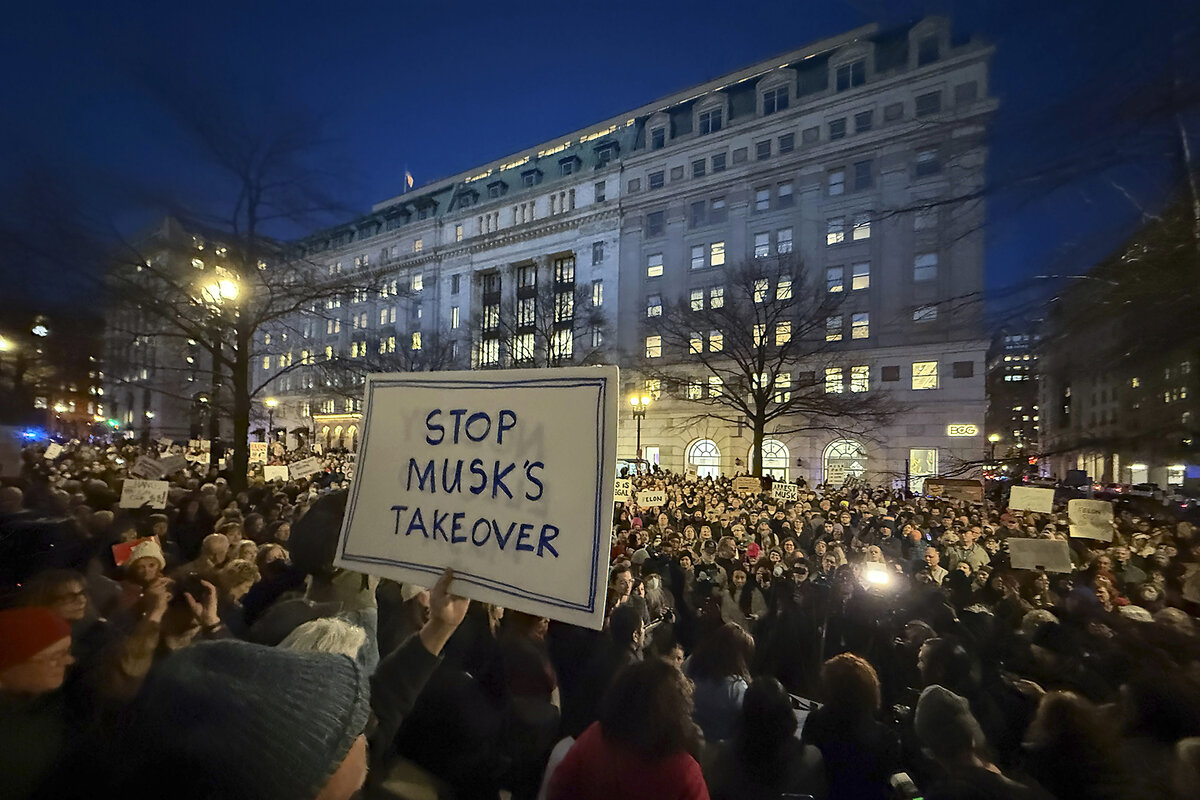 A large crowd gathers in the evening outside the Treasury building. One protester carries a placard that says "Stop Musk's Takeover."