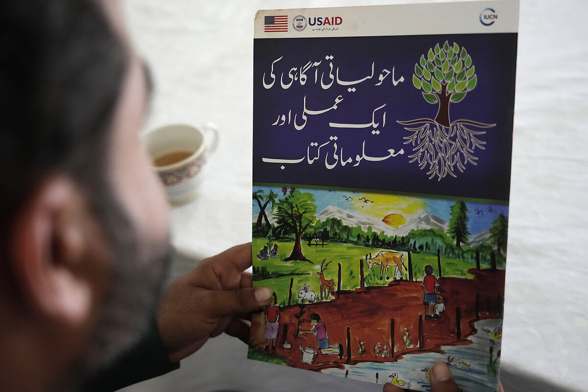 A young man is seen from behind, looking at a colorfully illustrated document about the environment.