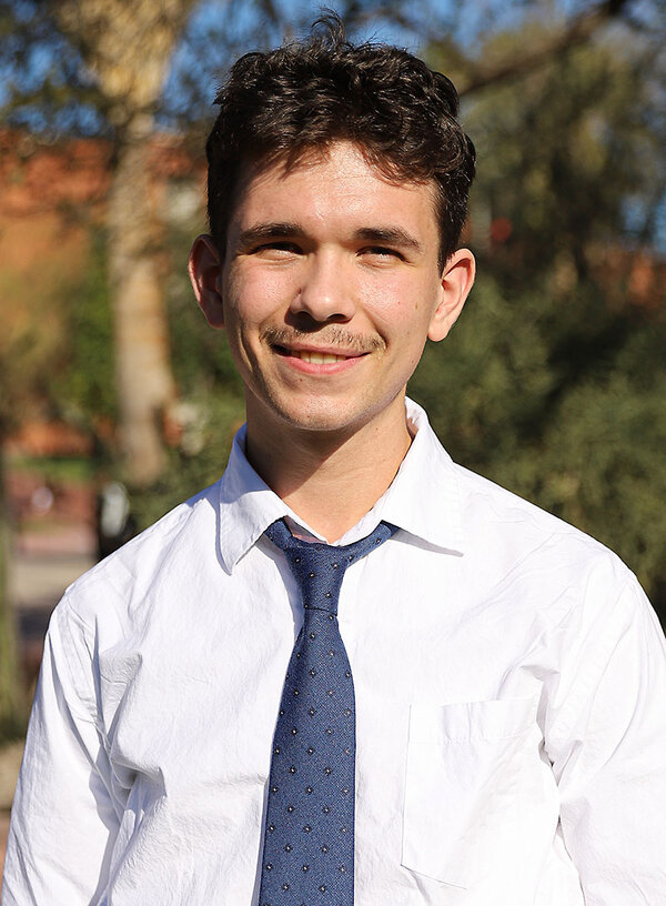 University of Arizona senior Maxwell Eller looks at the camera and smiles with the sun on his face and greenery behind him. 