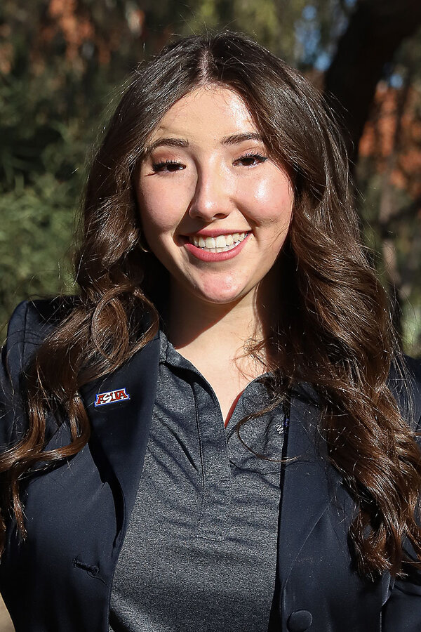 Liliana Quiroz, a senior at the University of Arizona, looks at the camera and smiles with the sun on her face and greenery behind her.