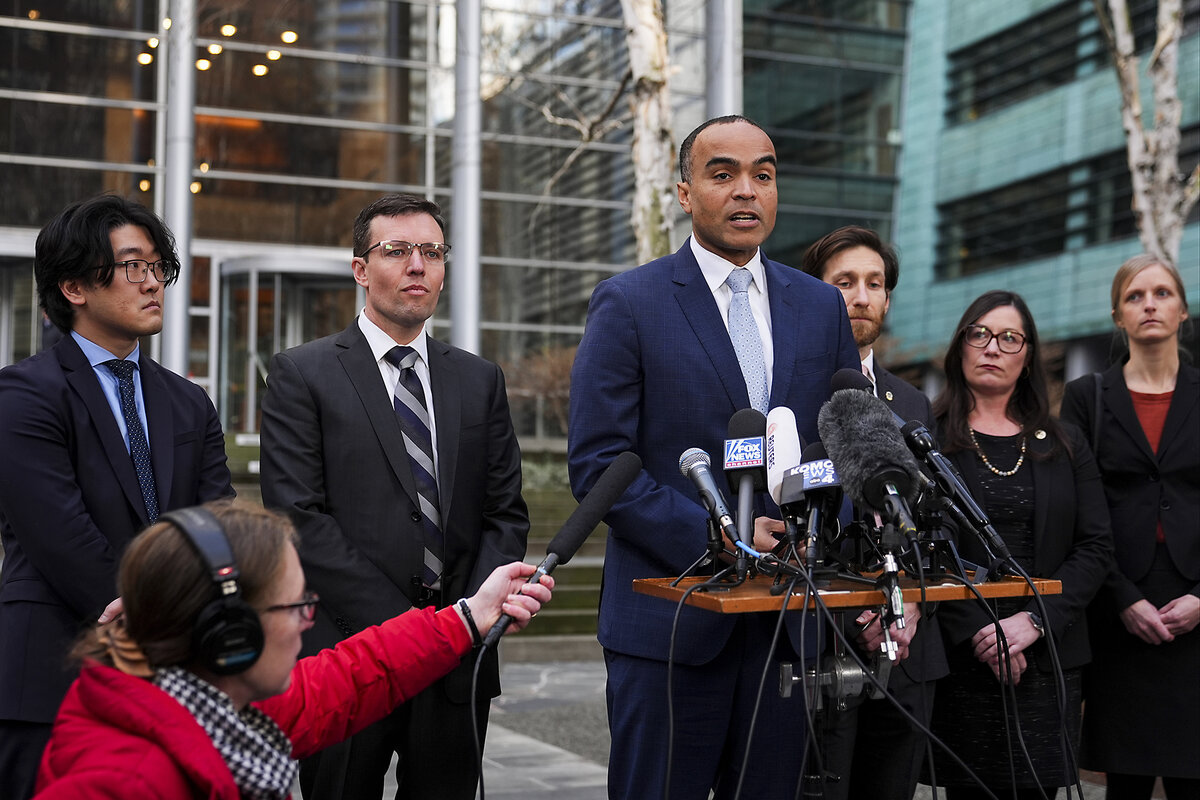 Washington Attorney General Nick Brown speaks into news media microphones at an outdoor podium in Seattle.