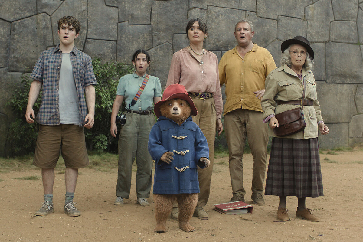 Paddington and his adoptive family stand with their backs facing a wall and their mouths open, is if in surprise