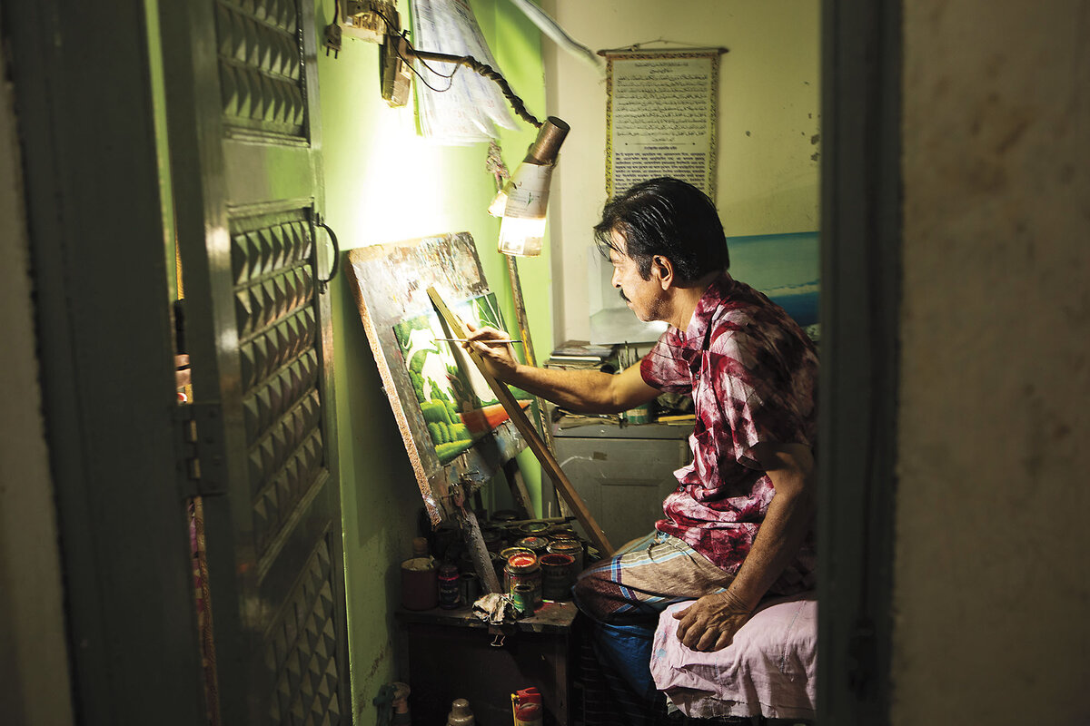 Syed Ahmed Hossain shines an electric lamp on his painting, propped against a wall, as he works in Old Dhaka, Bangladesh.
