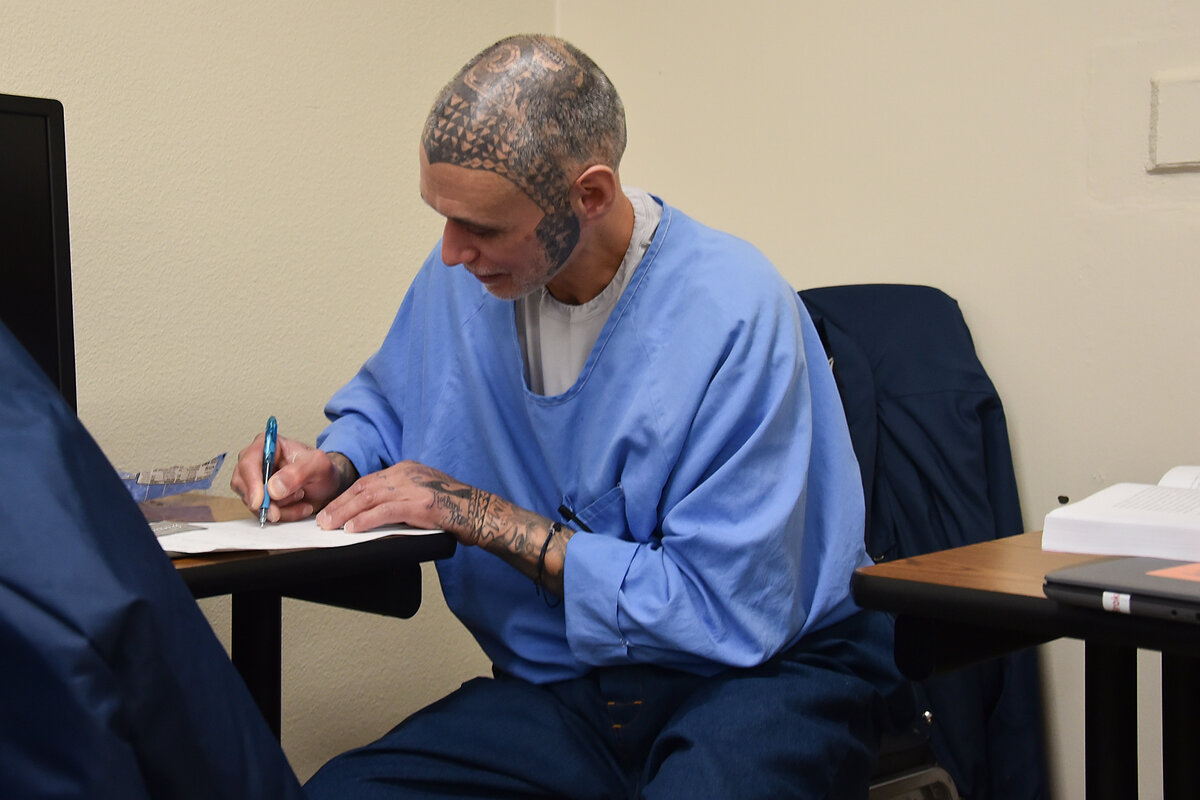 Pelican Bay State Prison student William Kaleipuakam Hopeau sits at a desk writing on papers in front of him.