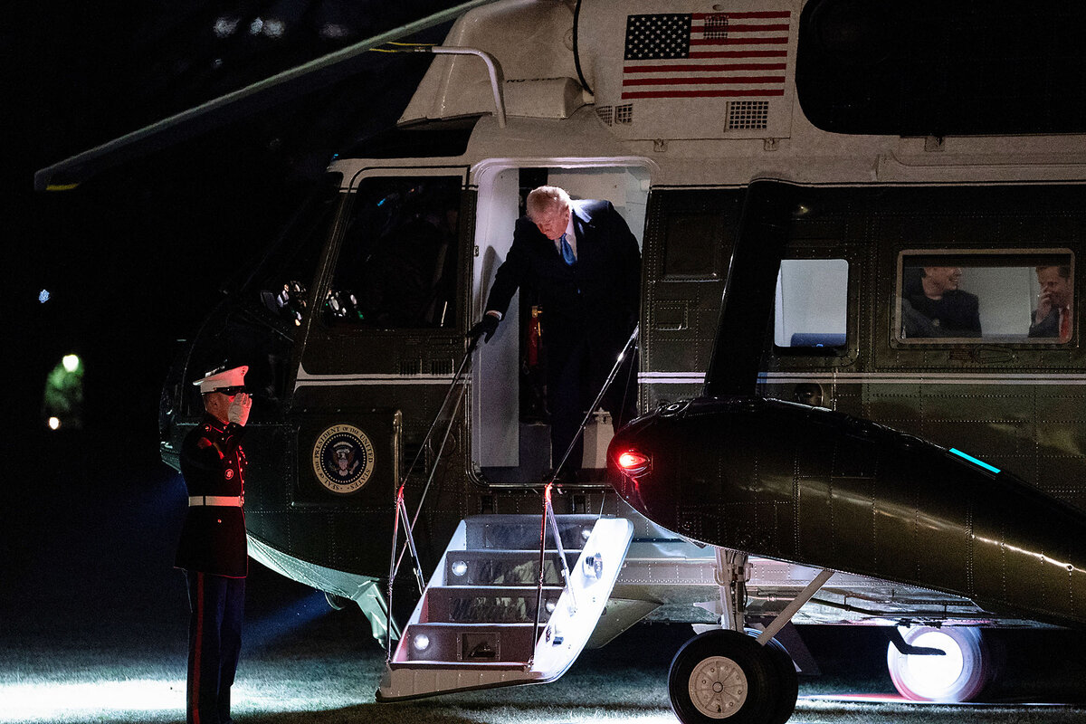 President Donald Trump, wearing a dark suit, grabs a railing as he descends a short staircase from the Marine One helicopter.