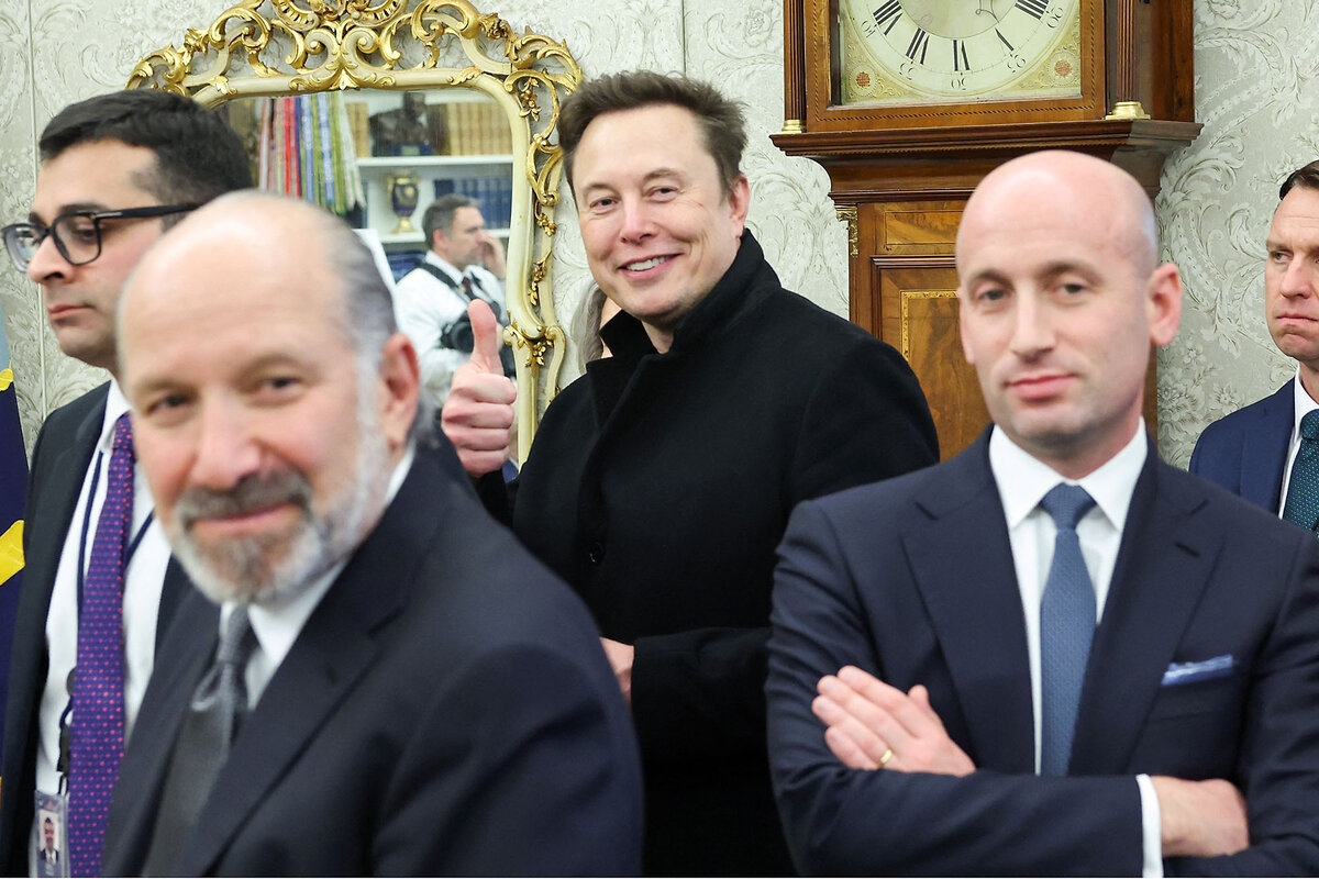 Elon Musk smiles, standing near other people inside the White House.