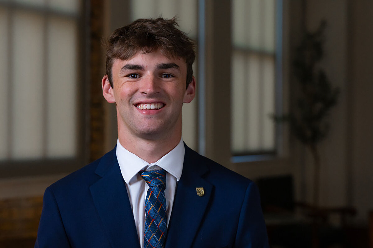 Student Jack Erickson, wearing a sport coat and tie, faces the camera and smiles
