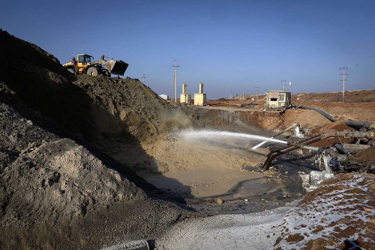 Machinery operates under a blue sky at an open pit mine.