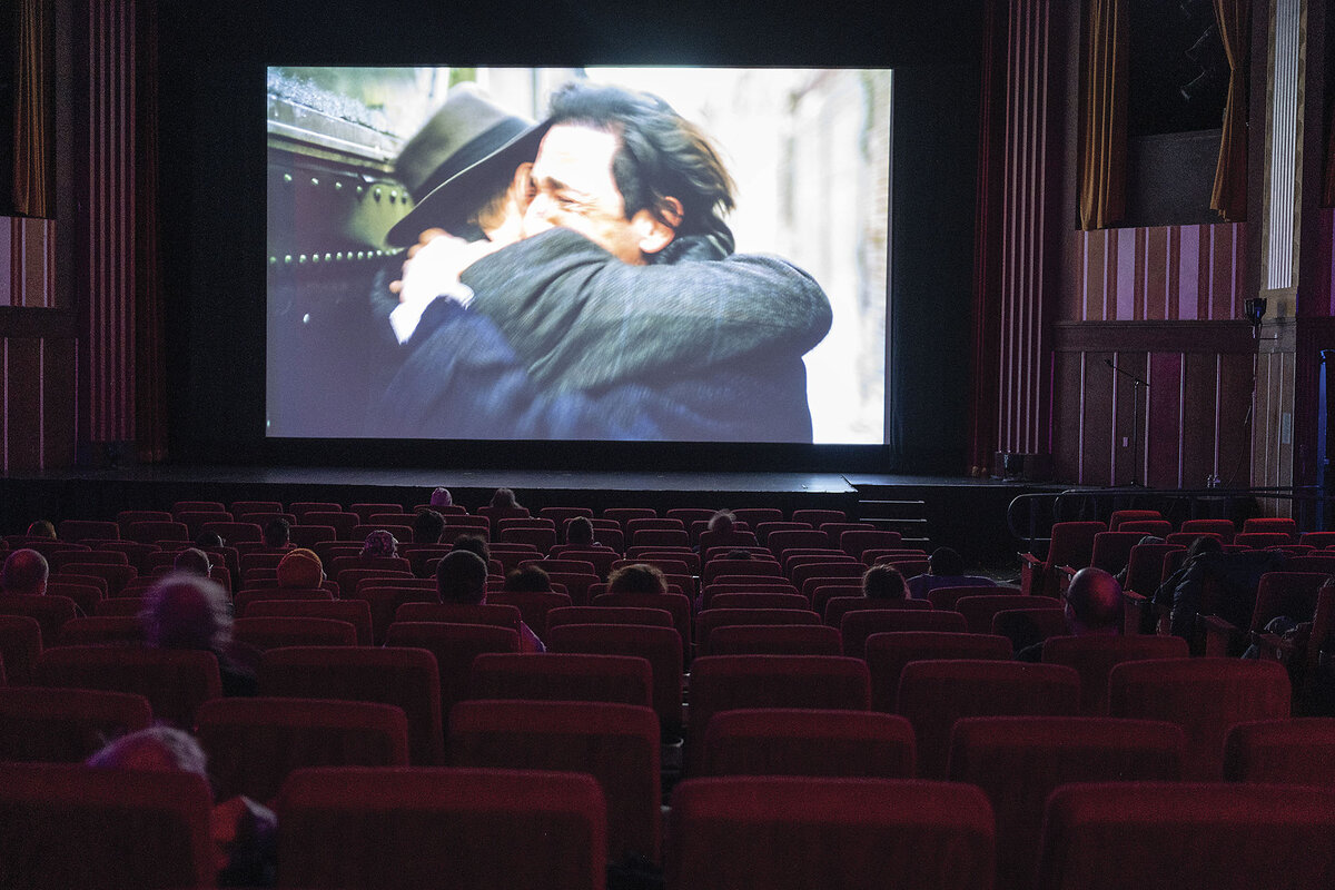 Two men embrace on screen in a darkened movie theater.