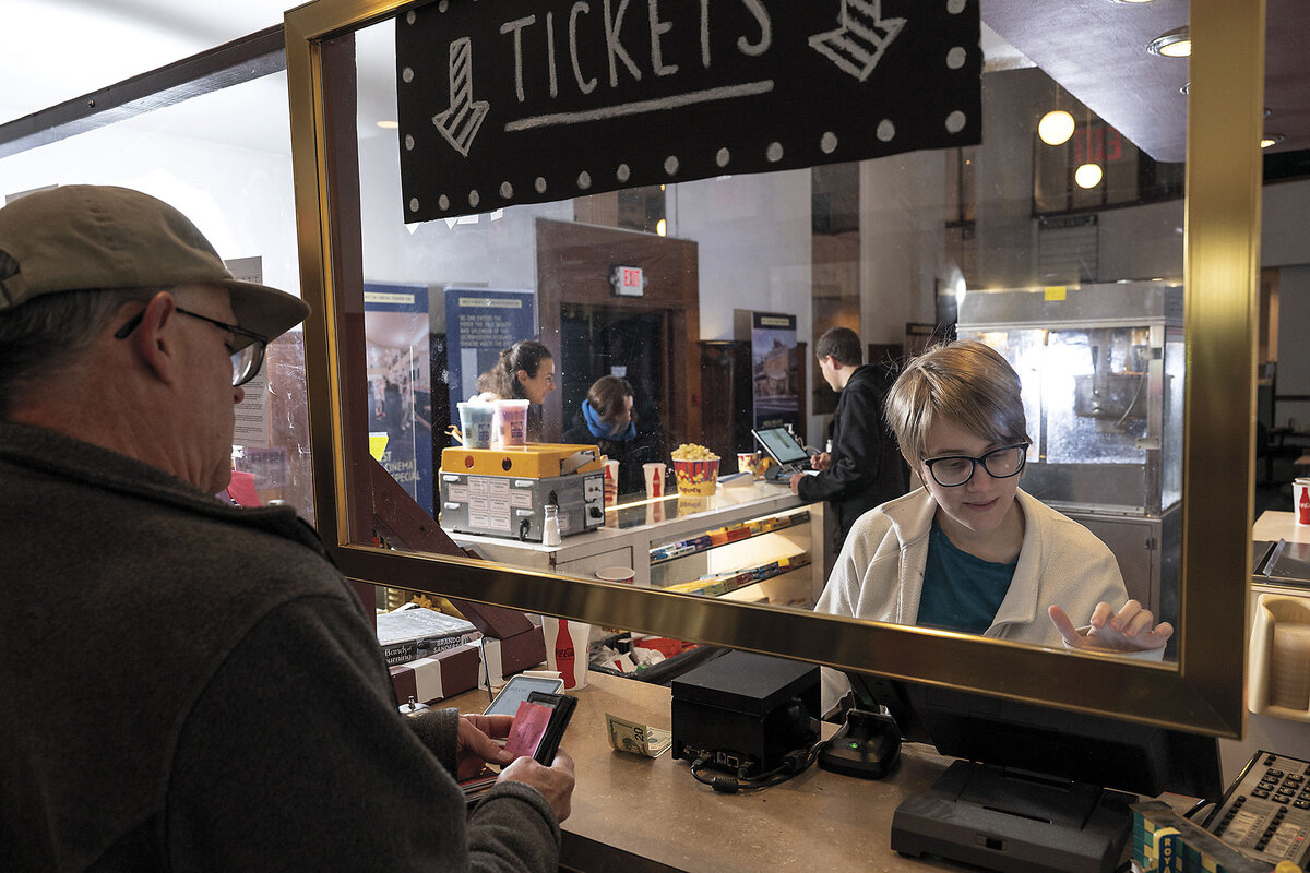 A woman stands behind a box office window with a sign reading 'tickets'