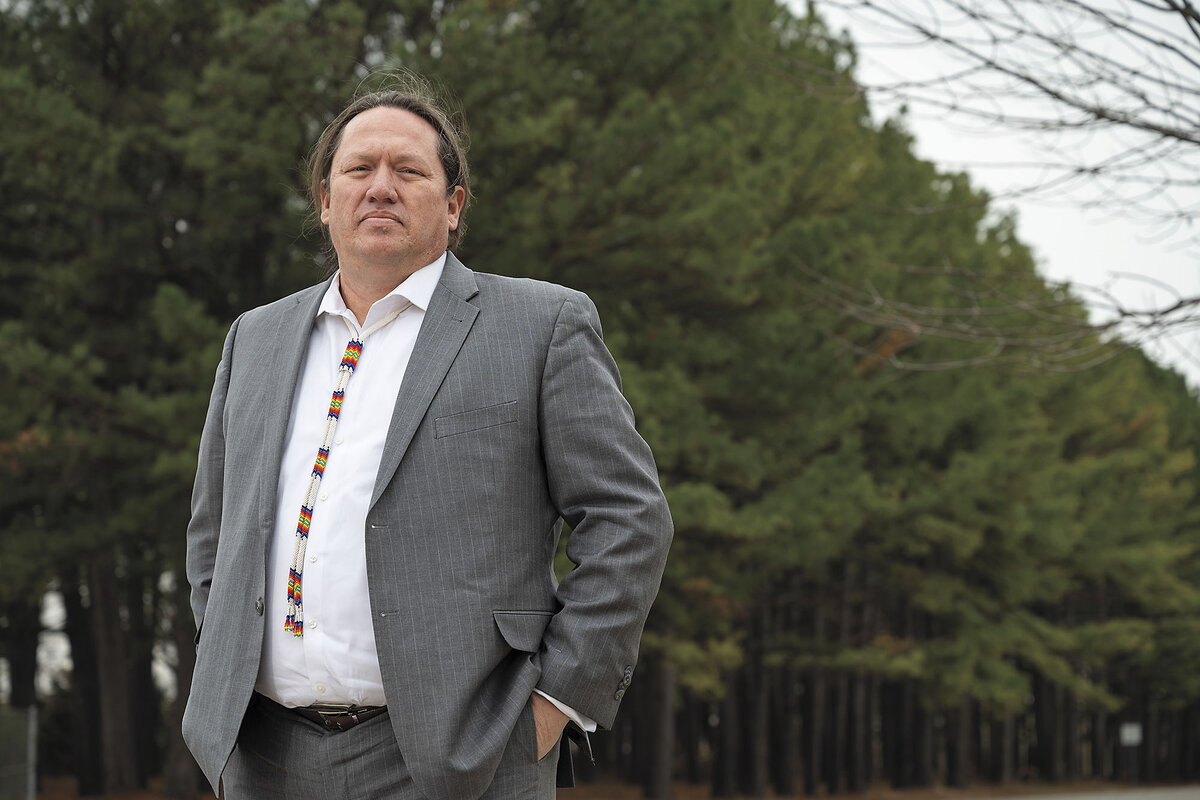 Chief Ben Barnes stands in front of pine trees, wearing a gray suit and a beaded tie.