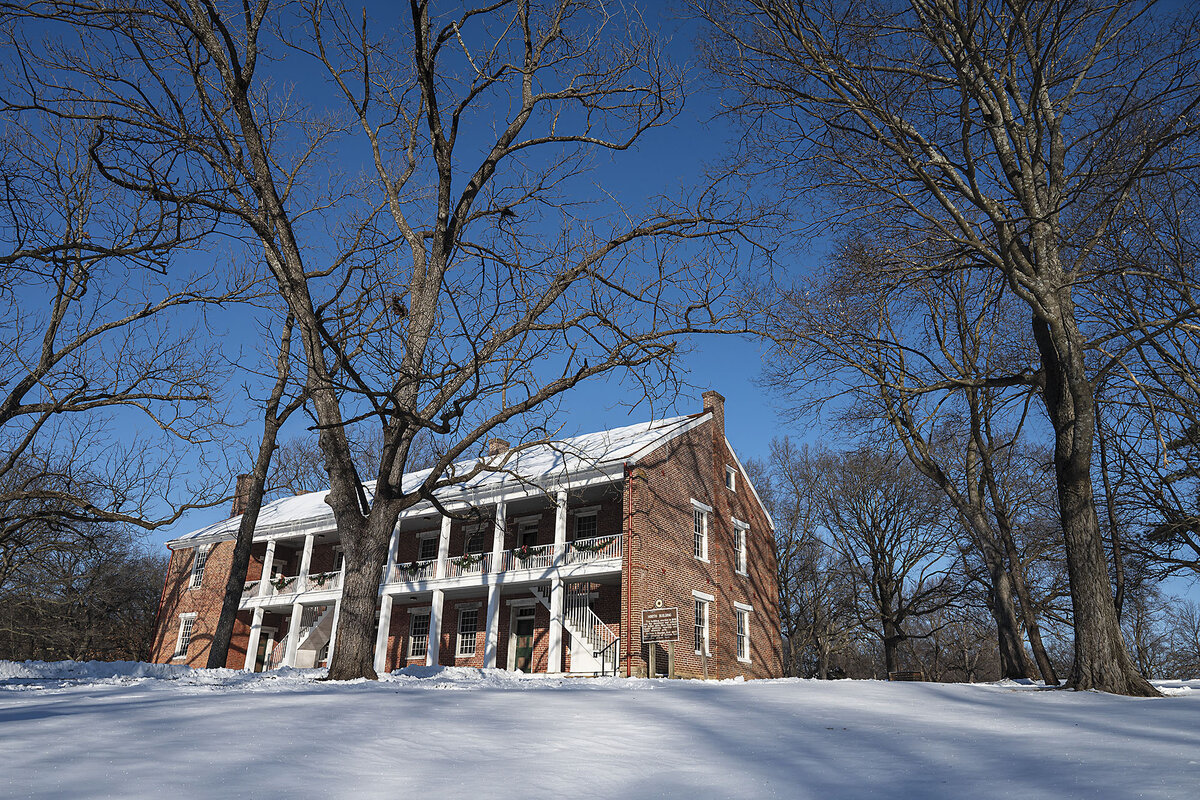 A brick building with a white pillared balcony sits atop a snow-covered hill.