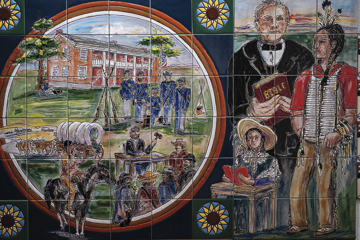 A tile mural depicts Civil War soliders, a Native American atop a horse, a covered pioneer wagon, and a minister preaching the Bible to a man in tribal dress.