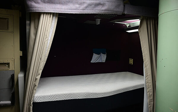 A single unmade bed is seen with privacy curtains pulled to either side.
