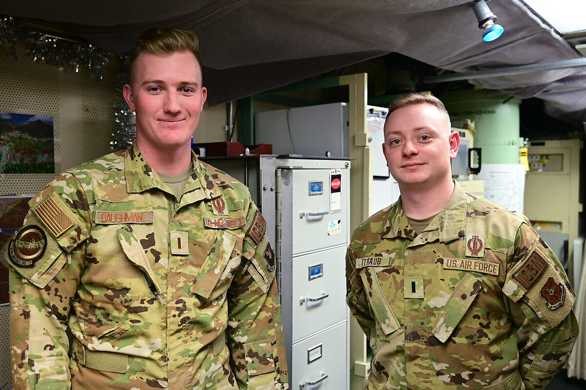 Two missileers wearing fatigues pose in front of a file cabinet.