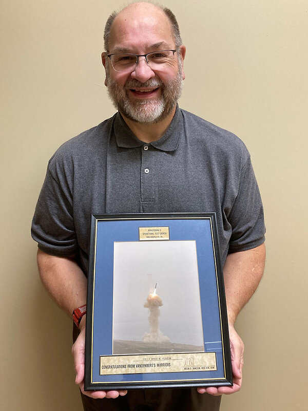 Former missileer David Feddern smiles holding a framed photograph of a missile launch.