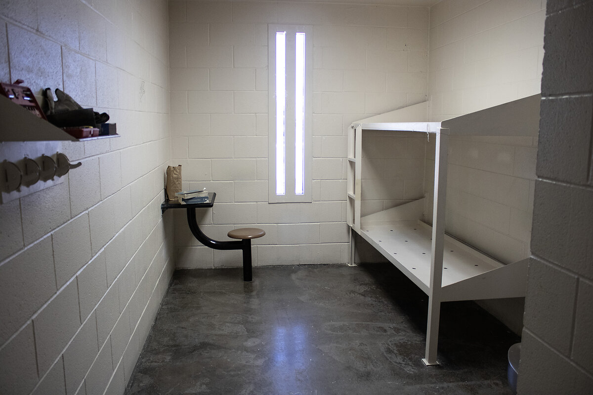 A room in a detention facility has a narrow window and white-painted cinder block walls.