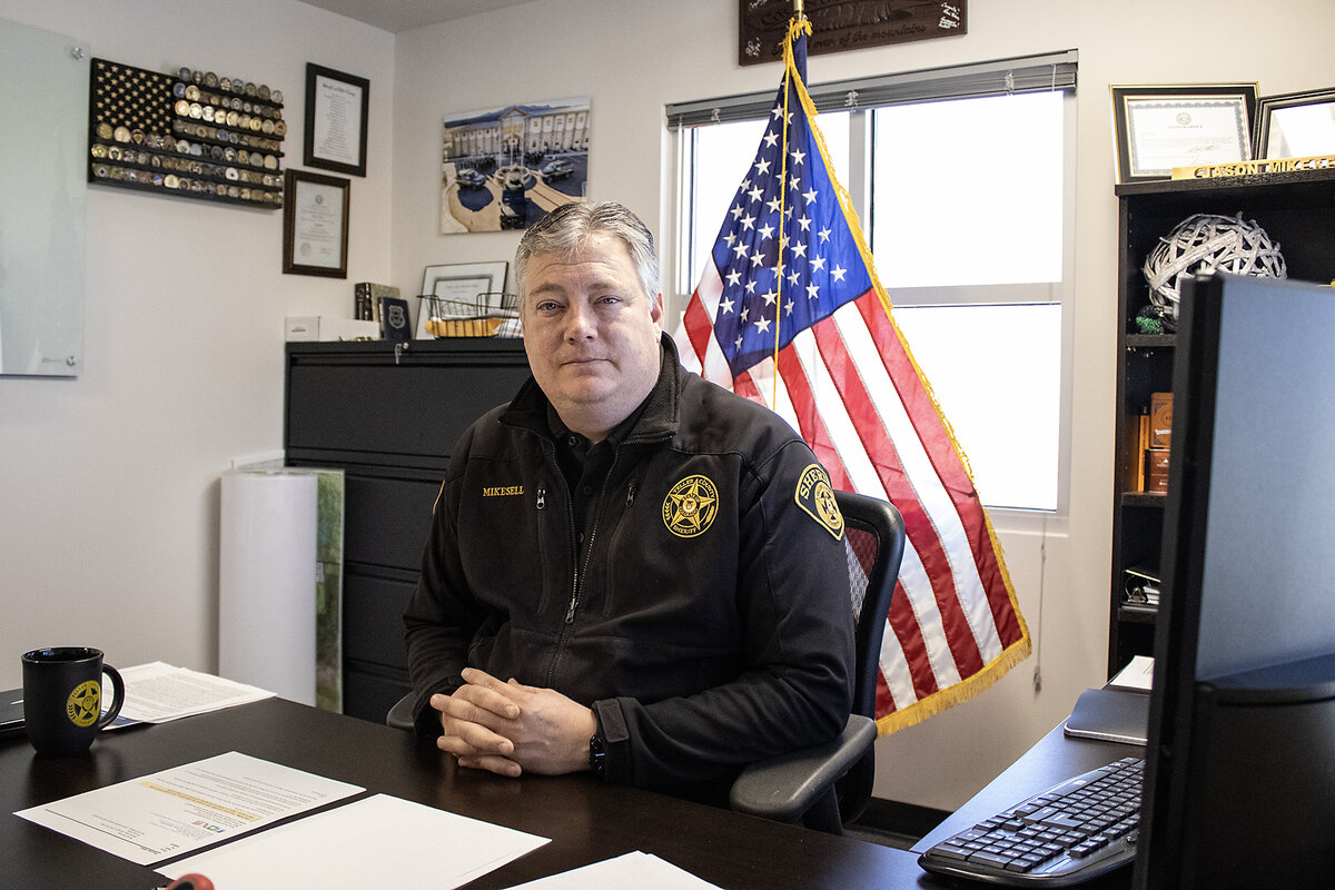 Sheriff Jason Mikesell, in a dark uniform, has an American flag behind his desk.