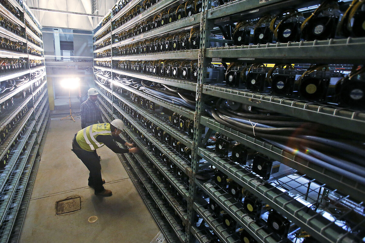 Two workers in safety vests examine tall racks filled with computer equipment.