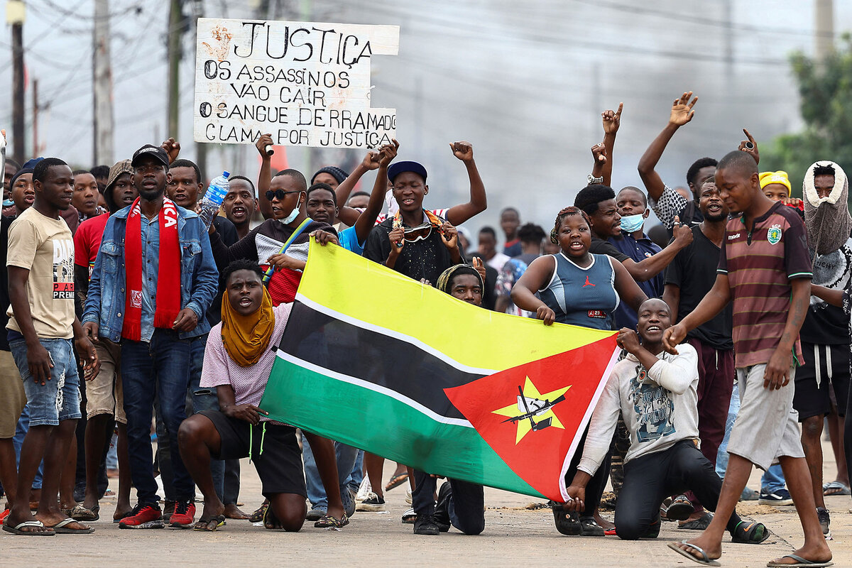 Protesters hold a sign and a Mozambique flag outdoors.