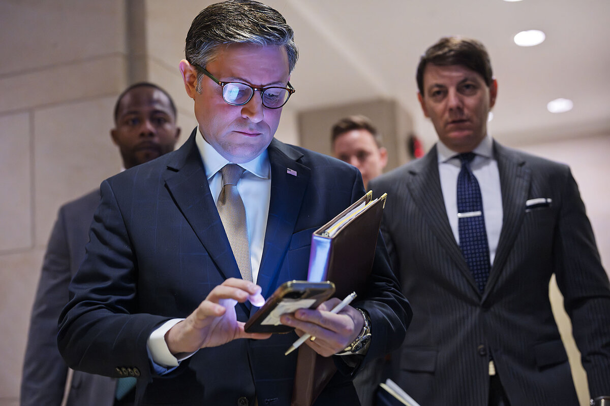 Speaker of the House Mike Johnson checks his cellphone in a hallway before meeting with reporters 