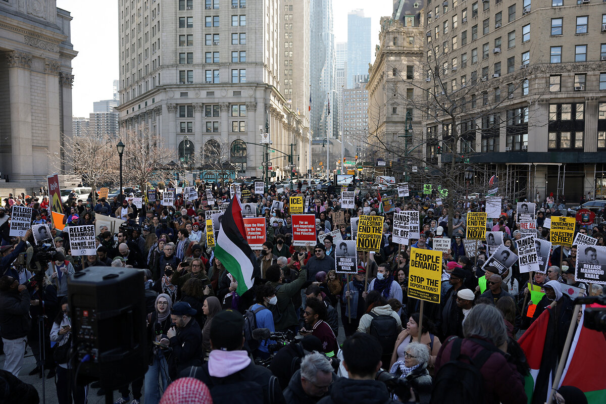 A large crowd gathers outdoors, with tall city buildings in the background.