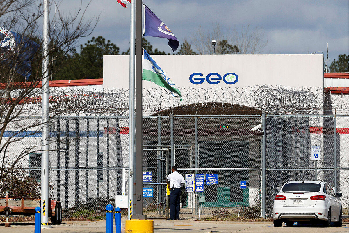 People stand near the entrance to a building that is surrounded by a high metal fence.