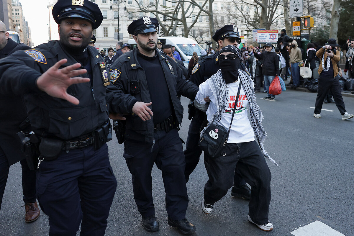 Uniformed police escort a masked protester who is being detained.