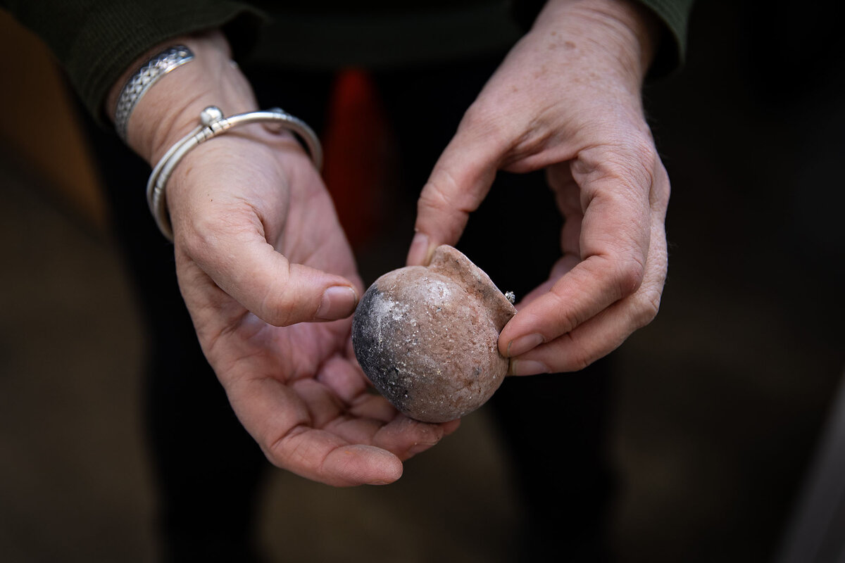 Nicole Moore's hands cradle a small, earth-toned ceramic pot from Senegal.