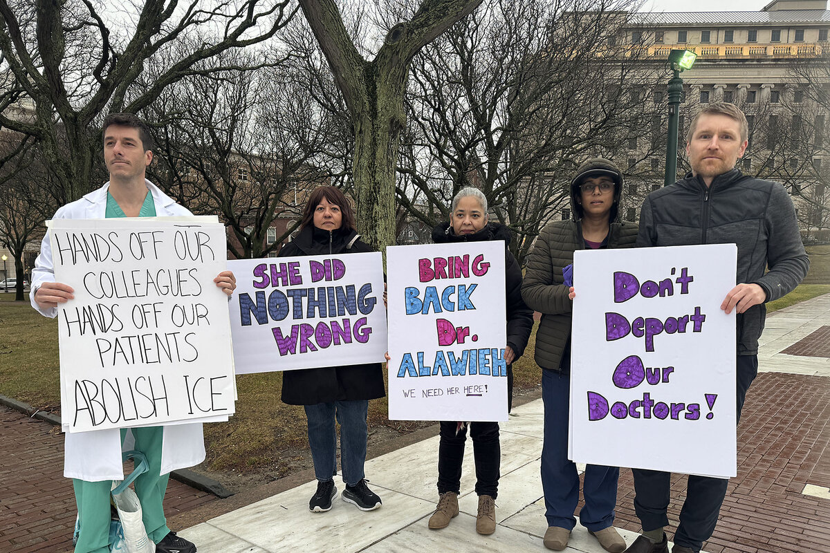 Health care workers hold signs outdoors in support of Dr. Rasha Alawieh.