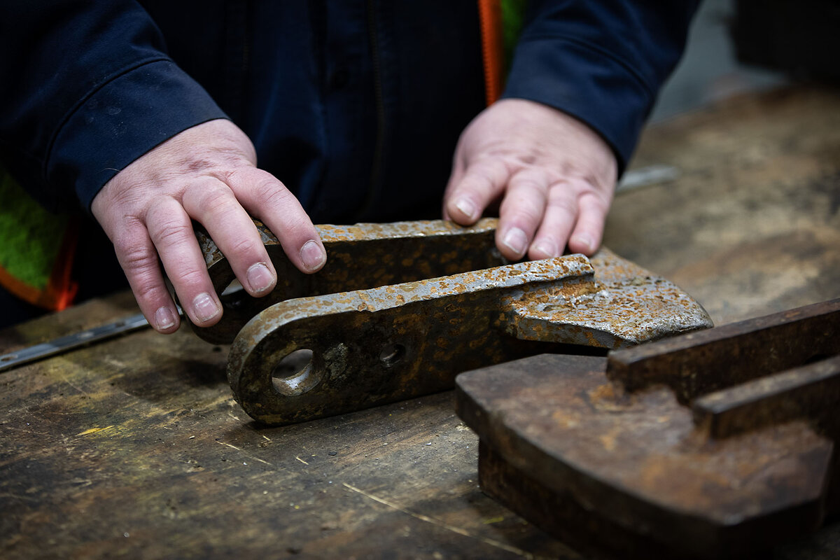Hands rest on a worn 10-pound iron swing hammer used for instruction.