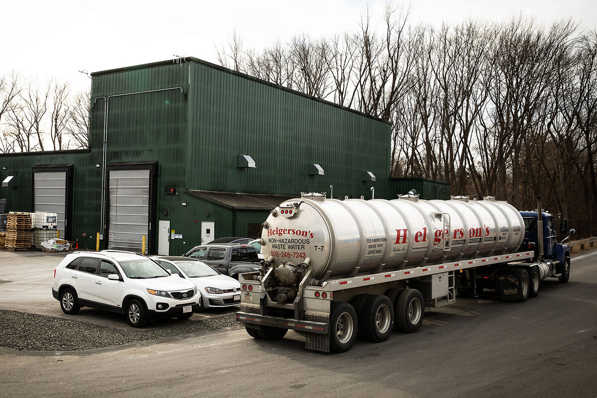 A tanker truck and a few cars sit outside a green industrial building.