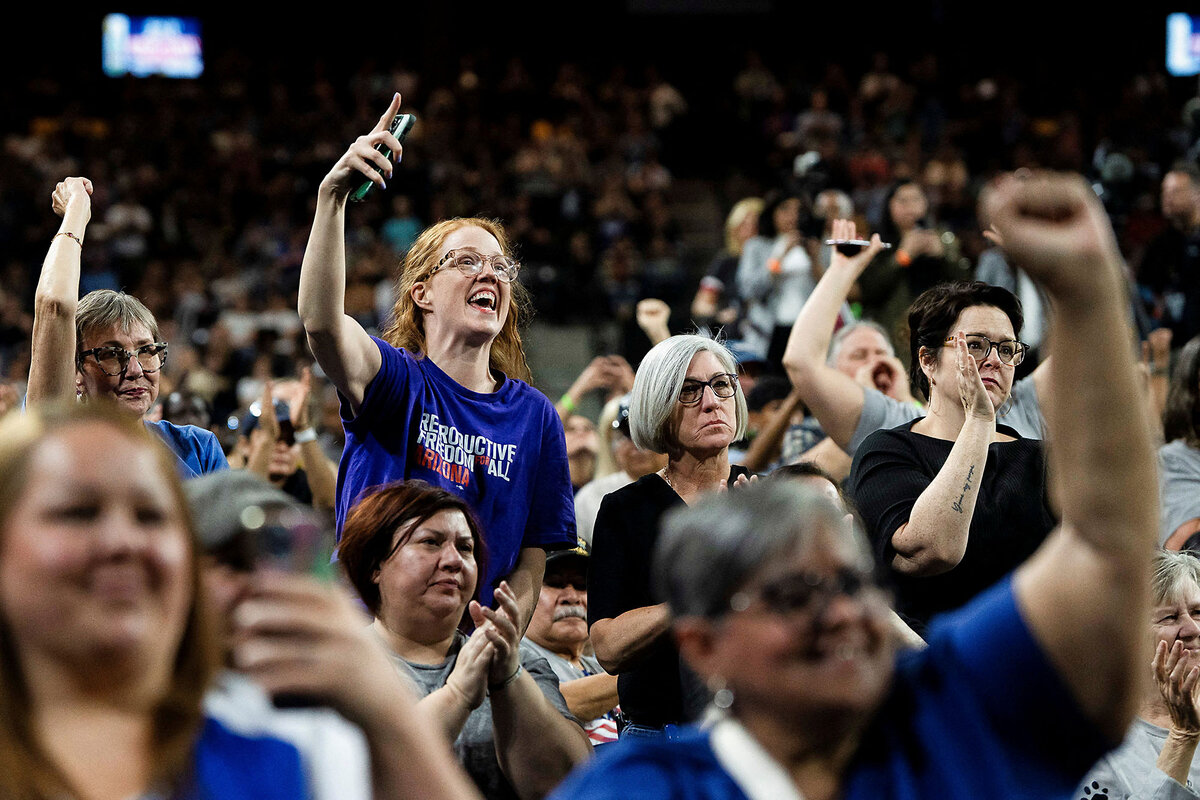 People cheer and smile in a large crowd.