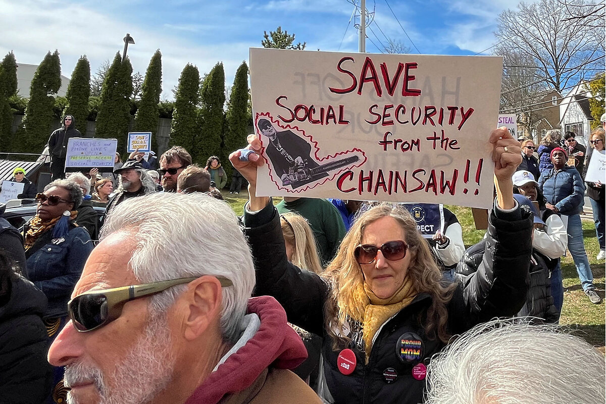 A woman in an outdoor crowd of protesters holds up a sign that says, 'Save Social Security from the Chainsaw.'